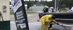 Crow wing county staff washing the bottom of a boat on a trailer with a power washer