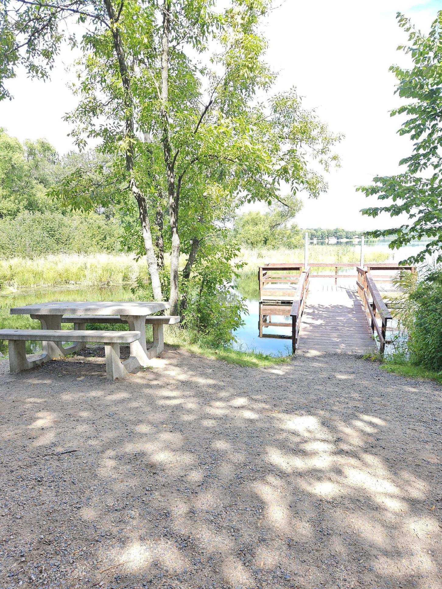 A green sign reads \"South Long Lake Park\" in white lettering. A paved area is backed by trees.